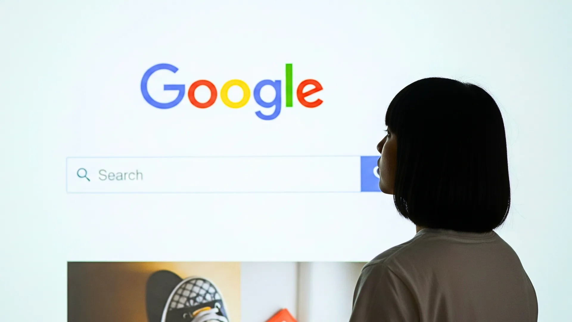 A person standing in front of a large screen displaying the Google search homepage, symbolizing internet browsing and search engine use.