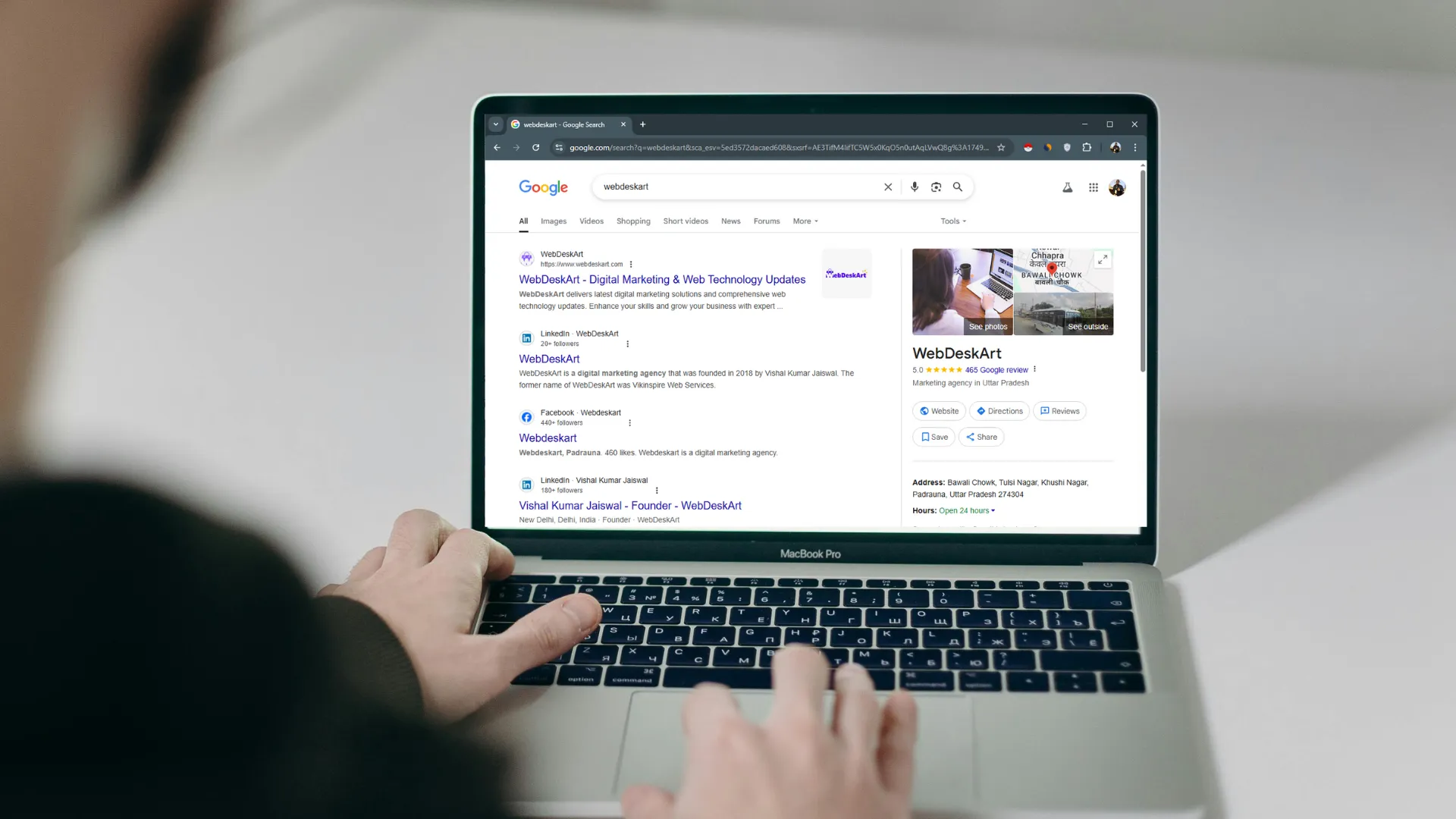 Person using MacBook Pro to search 'WebDeskArt' on Google, showing business profile and website of WebDeskArt.